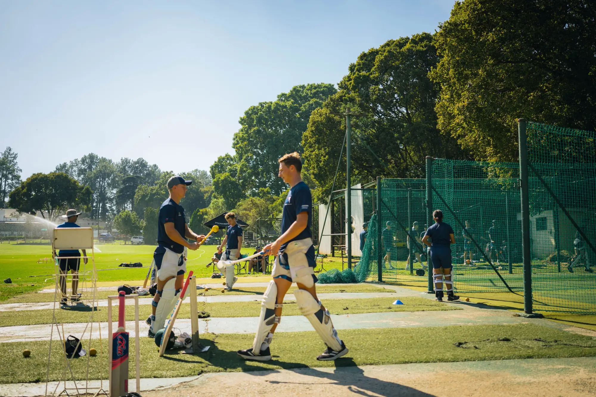 SSE batters in pads walking between the outdoor nets at training