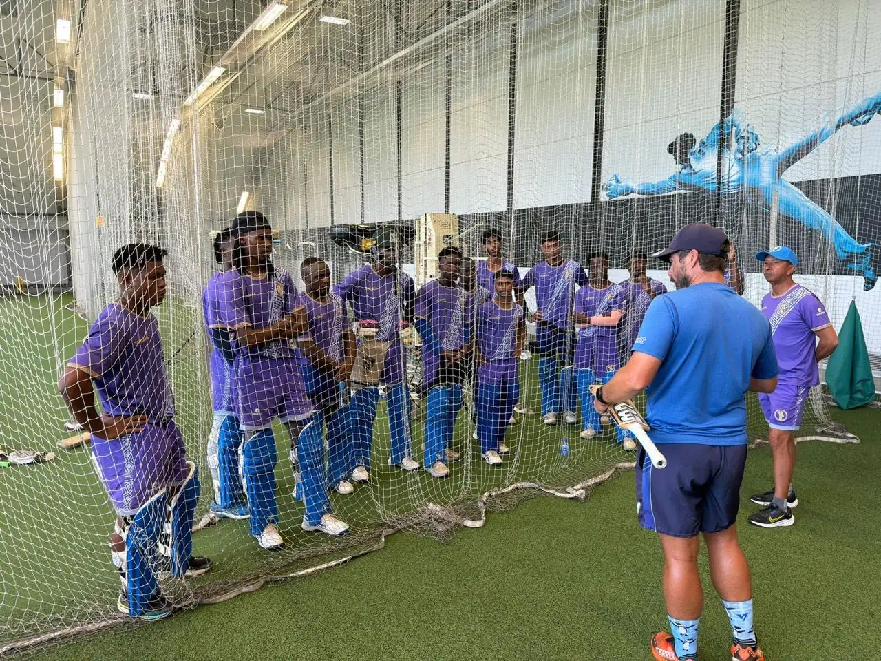 Coach briefing a touring squad in the indoor nets before a session