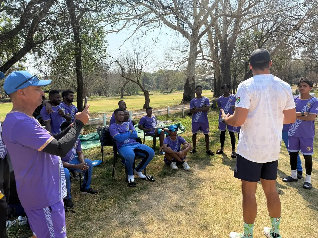 Coach giving a touring squad a team talk under the trees