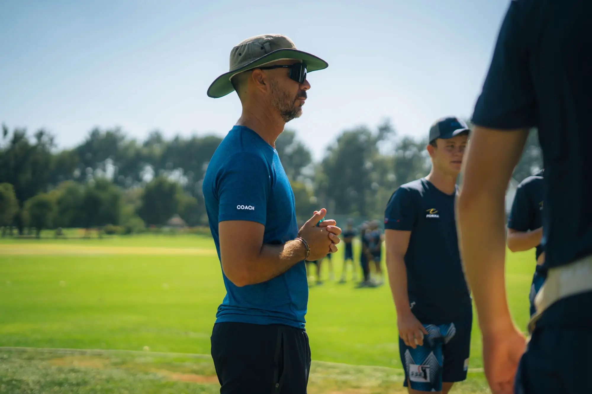 SSE coach in a sun hat talking with players on the training field