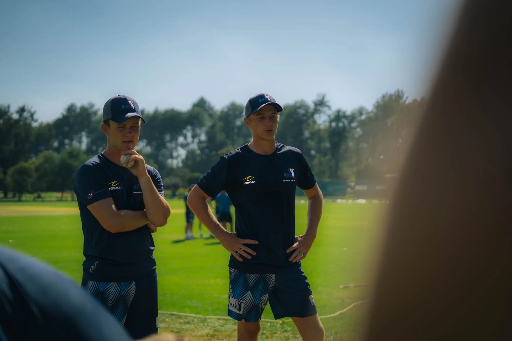 Two SSE players in caps watching a training session
