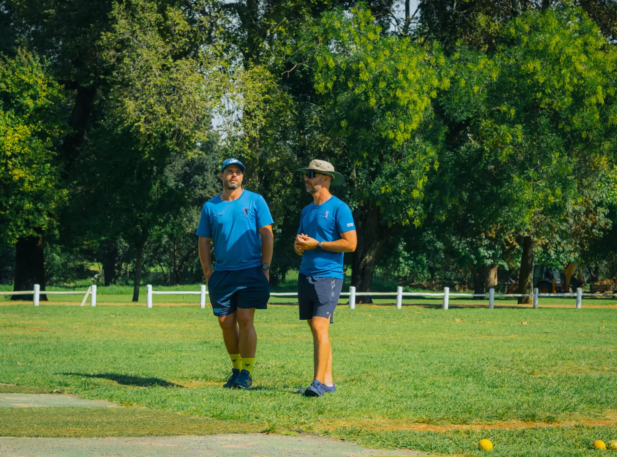 Two SSE coaches in blue kit talking on the training field